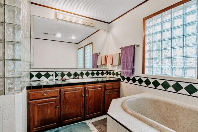 bathroom with crown molding, tile patterned flooring, vanity, tile walls, and a bath