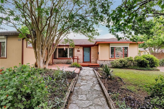 single story home featuring a front yard, stone siding, and stucco siding