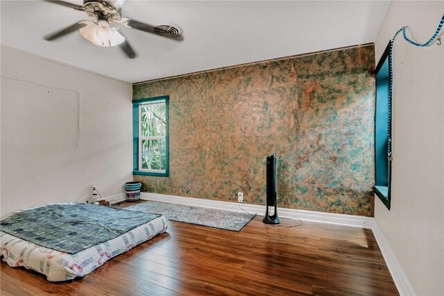 bedroom with a ceiling fan, baseboards, visible vents, and wood finished floors