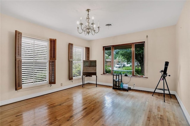 empty room with an inviting chandelier, baseboards, wood-type flooring, and visible vents