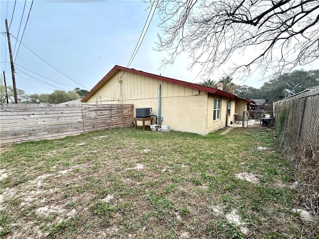 view of side of property with a fenced backyard, central AC, a chimney, a lawn, and brick siding