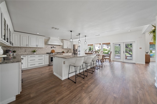 kitchen featuring stone counters, an island with sink, stainless steel stove, dark hardwood / wood-style floors, and premium range hood