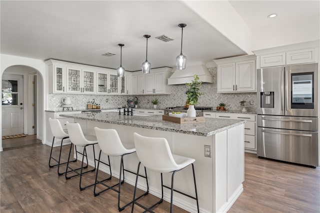 kitchen featuring an island with sink, custom range hood, dark wood-type flooring, and appliances with stainless steel finishes