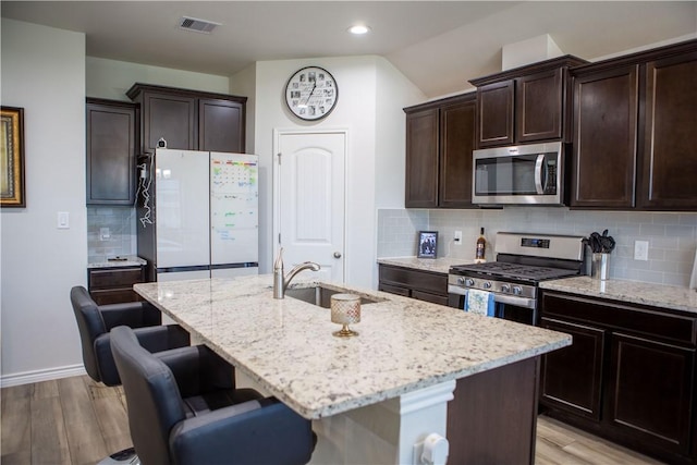 2682 Excelsior Blvd, Corpus Christi, TX 78415 - kitchen featuring stainless steel appliances, a sink, light wood finished floors, light stone countertops, and a center island with sink