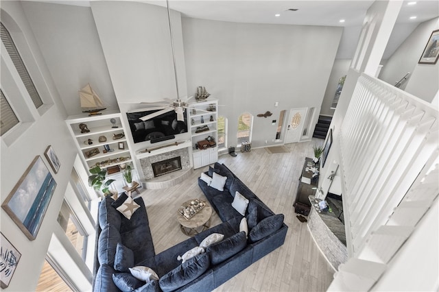 living room with a high ceiling, ceiling fan, a tile fireplace, and light hardwood / wood-style floors