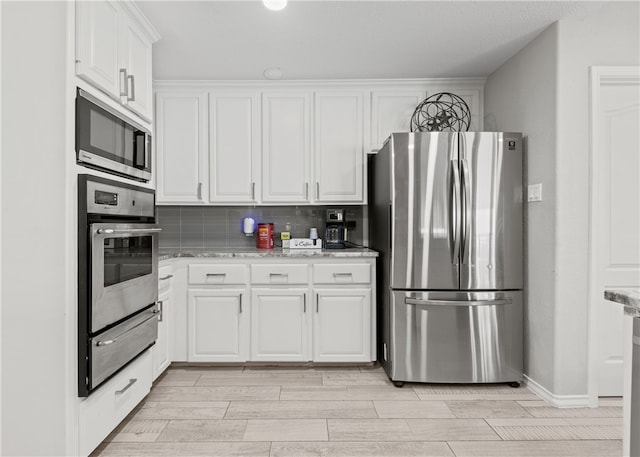 kitchen with tasteful backsplash, white cabinets, light stone counters, and stainless steel appliances