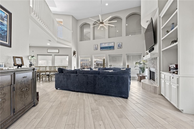 living room featuring light hardwood / wood-style floors, ceiling fan, a high ceiling, and a tile fireplace