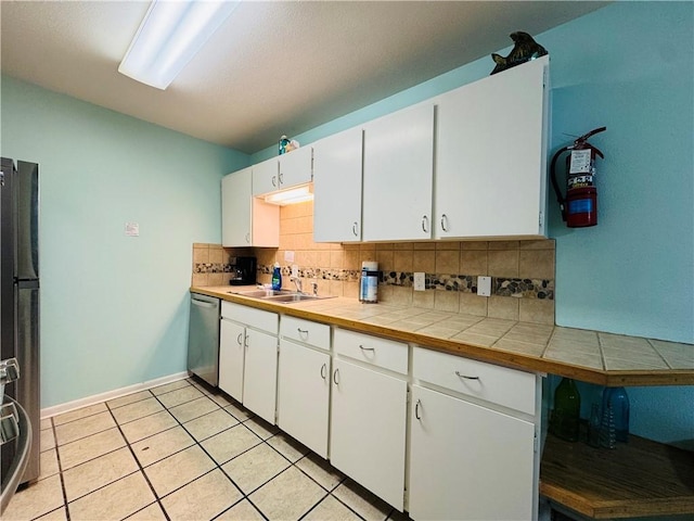 kitchen with sink, tile counters, light tile patterned flooring, white cabinetry, and stainless steel appliances