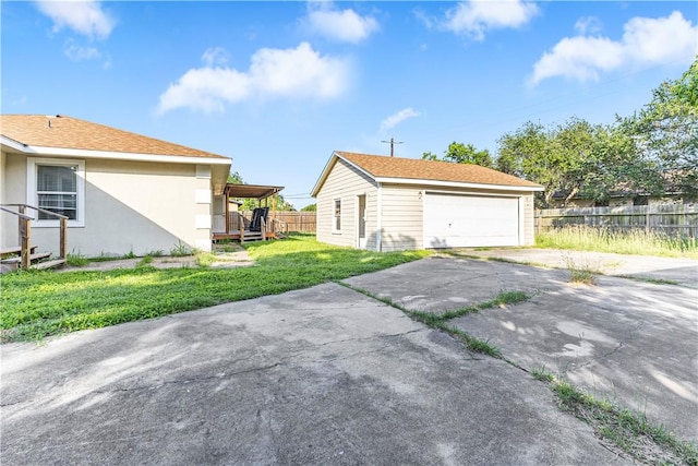 view of side of home with a garage, fence, stucco siding, a yard, and an outbuilding