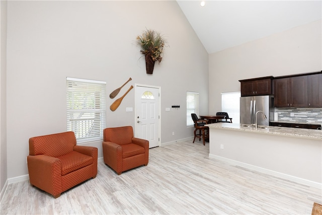 sitting room featuring high vaulted ceiling, sink, and light wood-type flooring