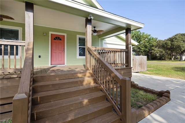entrance to property with a lawn, ceiling fan, and covered porch