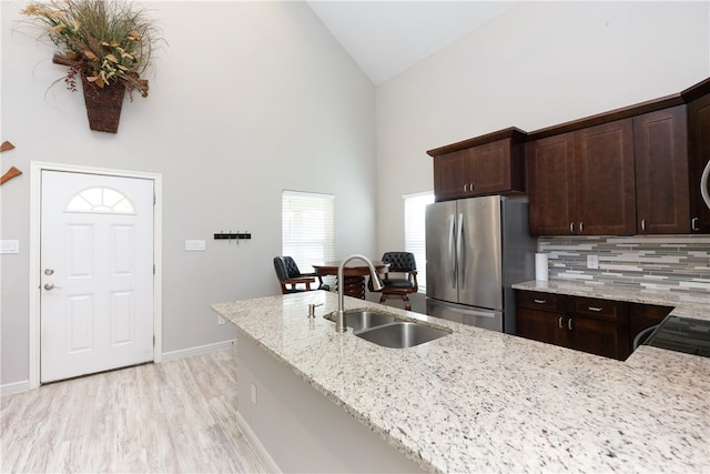 kitchen with light stone counters, dark brown cabinets, stainless steel refrigerator, sink, and light hardwood / wood-style flooring
