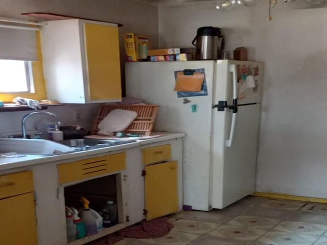 kitchen featuring freestanding refrigerator, light countertops, a sink, and light floors