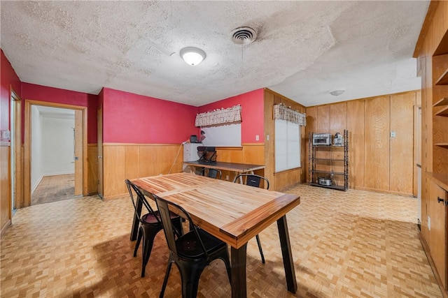 dining room with wood walls, a textured ceiling, and light parquet floors