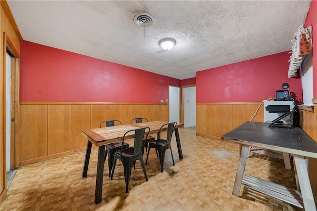 dining area with wooden walls, light parquet floors, and a textured ceiling