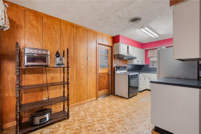 kitchen featuring white refrigerator, white cabinetry, wooden walls, and range with gas stovetop