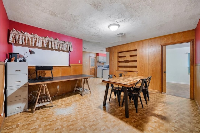 dining room with washer / clothes dryer, wooden walls, light parquet flooring, and a textured ceiling