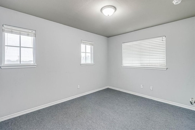 spare room featuring dark carpet and baseboards