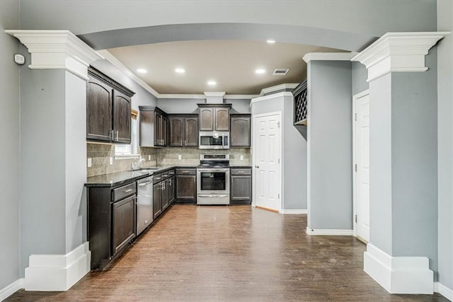 kitchen featuring decorative columns, tasteful backsplash, appliances with stainless steel finishes, dark brown cabinetry, and wood finished floors