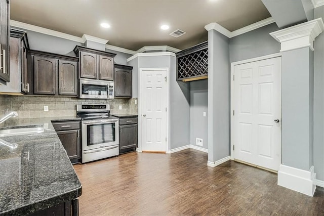 kitchen with dark brown cabinetry, decorative columns, appliances with stainless steel finishes, dark stone countertops, and a sink