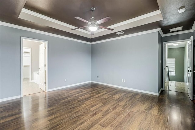 unfurnished bedroom featuring baseboards, visible vents, ornamental molding, dark wood-type flooring, and a tray ceiling