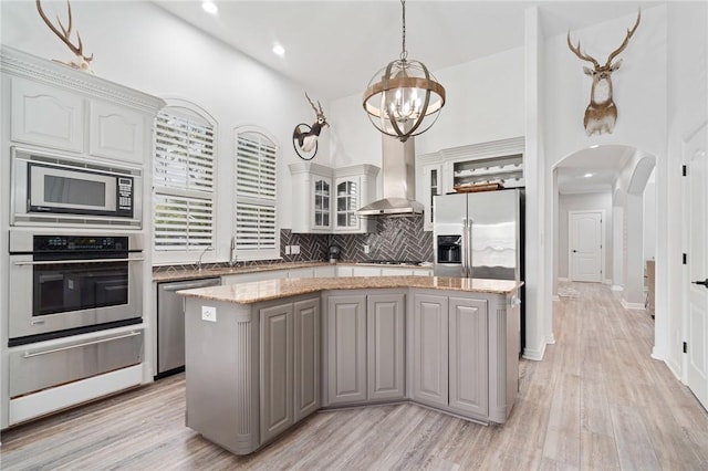 4589 Teal Dr, Corpus Christi, TX 78410 - kitchen featuring wall chimney exhaust hood, arched walkways, a center island, stainless steel appliances, and gray cabinetry