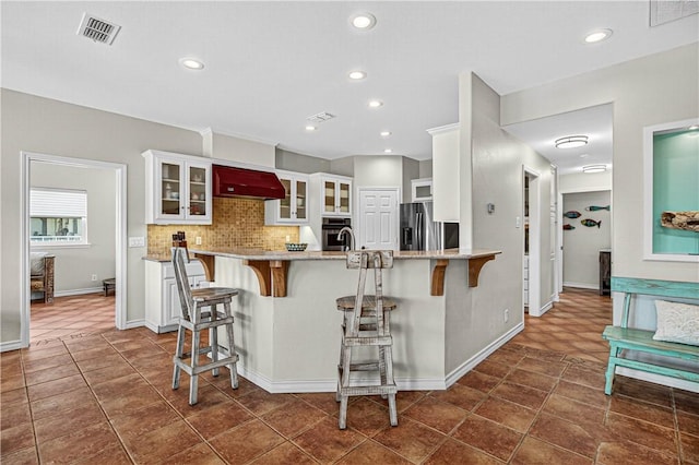 973 Pompano Dr, Aransas Pass, TX 78336 - kitchen featuring stainless steel appliances, custom range hood, tasteful backsplash, a peninsula, and white cabinetry