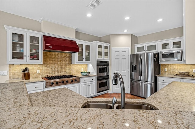 973 Pompano Dr, Aransas Pass, TX 78336 - kitchen with stainless steel appliances, custom range hood, tasteful backsplash, white cabinets, and light stone counters