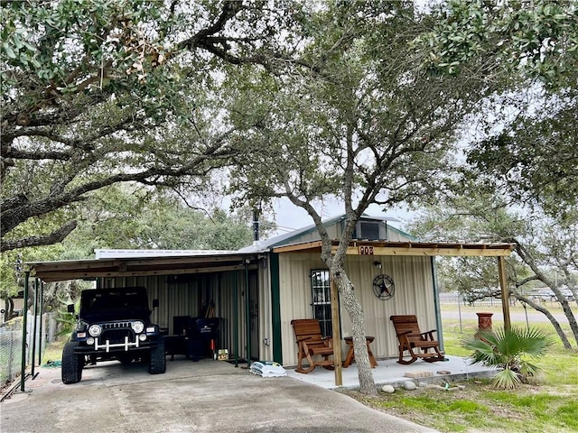 view of outdoor structure with concrete driveway, an attached carport, and fence