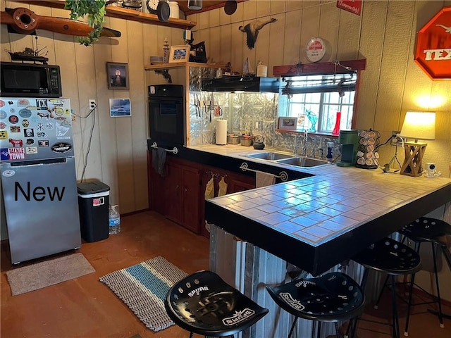 kitchen with tile countertops, a sink, black appliances, a peninsula, and a kitchen breakfast bar