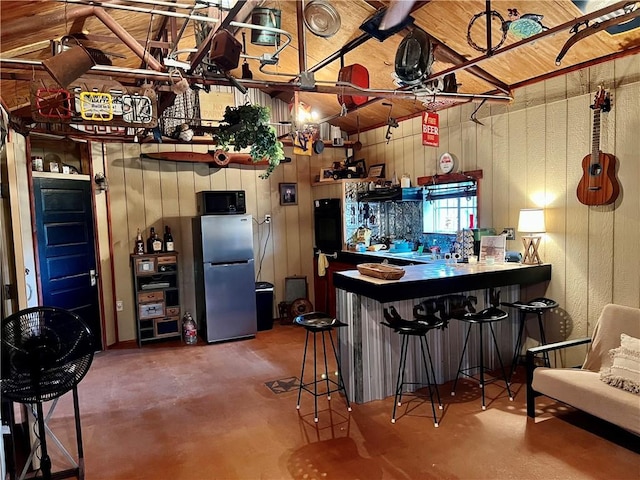 bar featuring black microwave, concrete floors, wood walls, freestanding refrigerator, and a dry bar