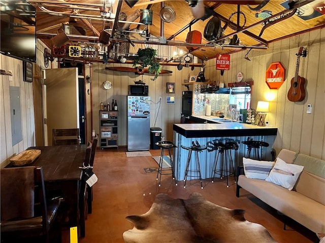 interior space featuring electric panel, freestanding refrigerator, concrete flooring, wood walls, and black microwave