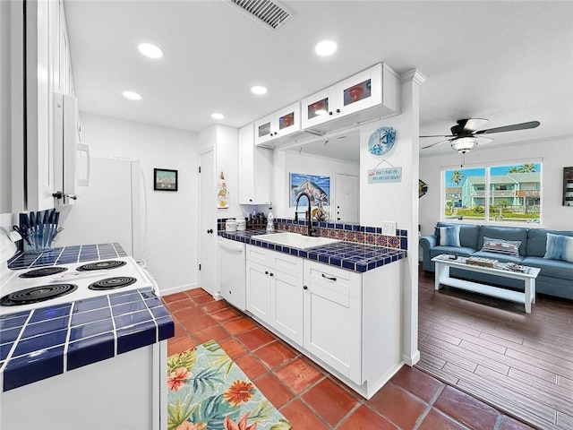 kitchen featuring a sink, tile counters, white cabinetry, visible vents, and glass insert cabinets