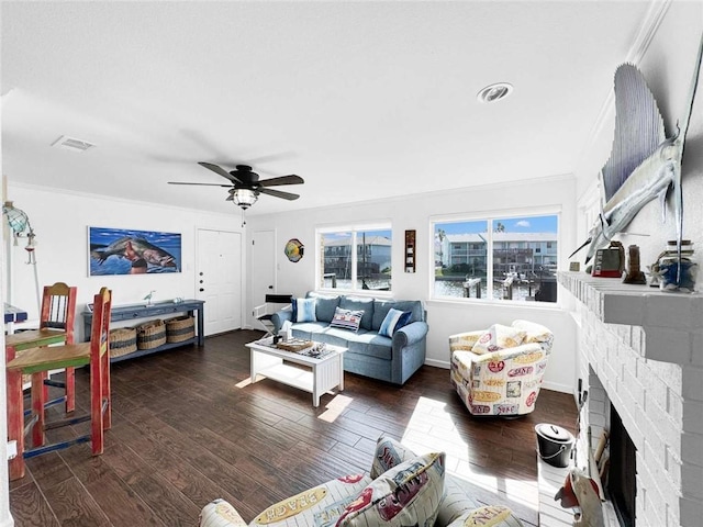 living area with ornamental molding, a brick fireplace, ceiling fan, and dark wood-style floors