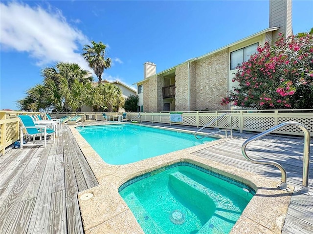 community pool featuring a hot tub, fence, and a wooden deck