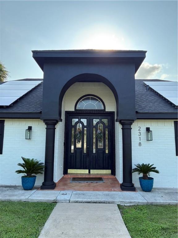 doorway to property featuring a shingled roof, brick siding, and french doors