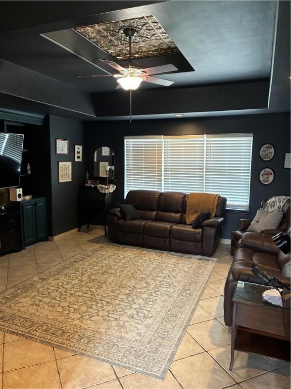 living room with a raised ceiling, light tile patterned flooring, and a ceiling fan