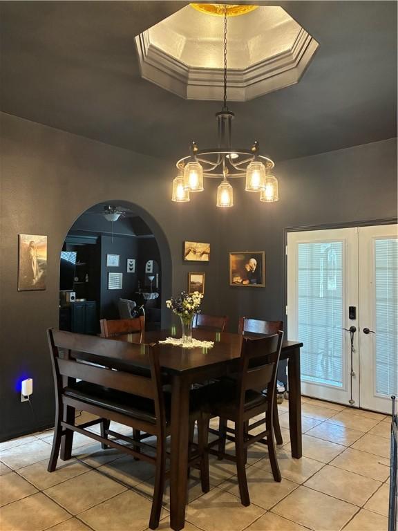 dining room featuring light tile patterned floors, a raised ceiling, arched walkways, and a chandelier
