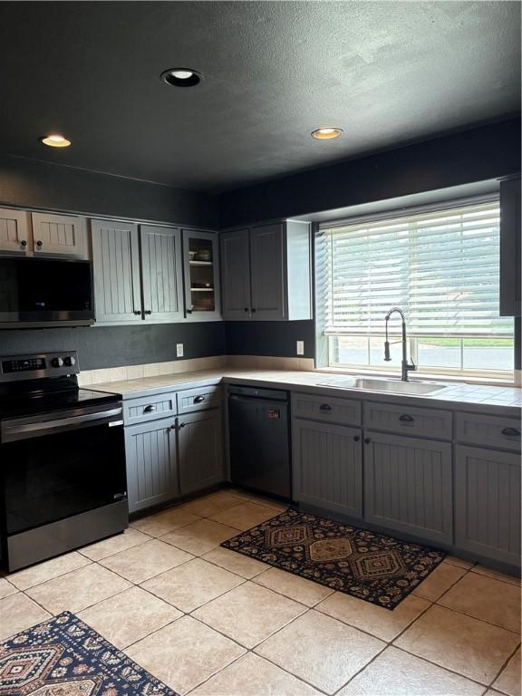 kitchen with stainless steel appliances, a sink, gray cabinets, light countertops, and a textured ceiling