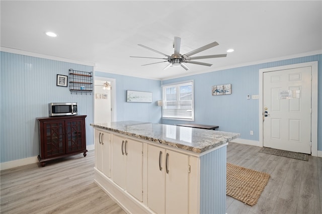 kitchen featuring ceiling fan, a kitchen island, ornamental molding, and light wood-type flooring