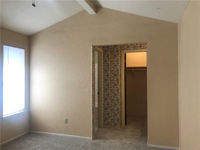 unfurnished bedroom with a textured wall, lofted ceiling with beams, carpet, a spacious closet, and a closet