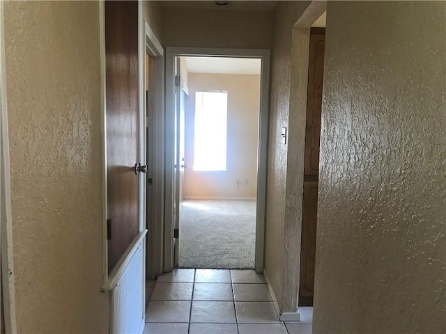 corridor featuring light tile patterned flooring, a textured wall, light carpet, and baseboards