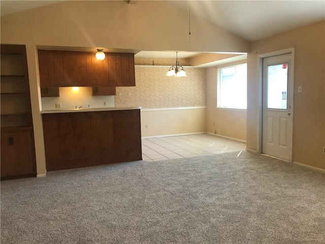 kitchen featuring lofted ceiling, pendant lighting, light colored carpet, and an inviting chandelier