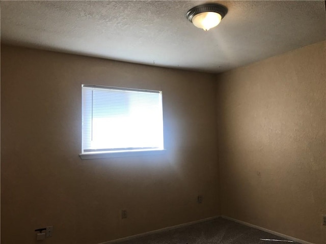 unfurnished room featuring baseboards, dark colored carpet, and a textured ceiling