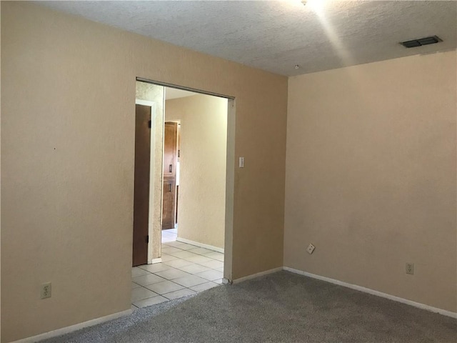 empty room featuring light tile patterned floors, baseboards, visible vents, light colored carpet, and a textured ceiling