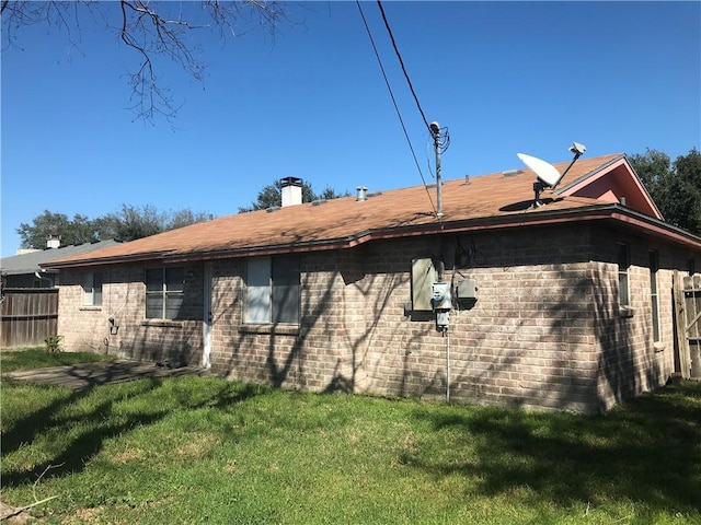 back of house with brick siding, a lawn, a chimney, and fence