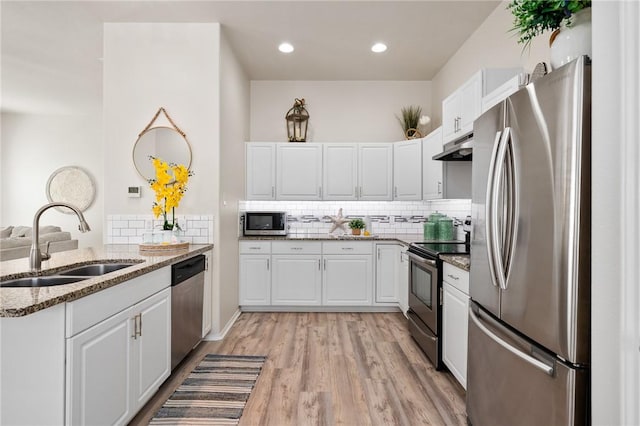 kitchen with light stone counters, a sink, stainless steel appliances, white cabinets, and under cabinet range hood