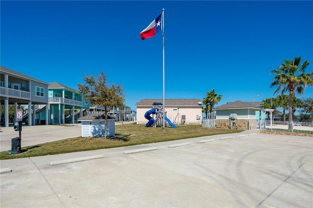 view of community featuring fence, concrete driveway, playground community, a lawn, and a carport