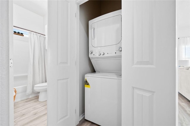 clothes washing area featuring stacked washer / dryer, laundry area, and wood finished floors