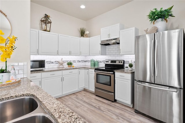 kitchen with under cabinet range hood, backsplash, appliances with stainless steel finishes, and light wood finished floors